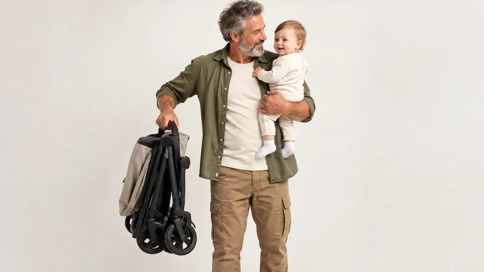 A parent lifting a folded compact stroller with one hand while holding a baby on the other arm