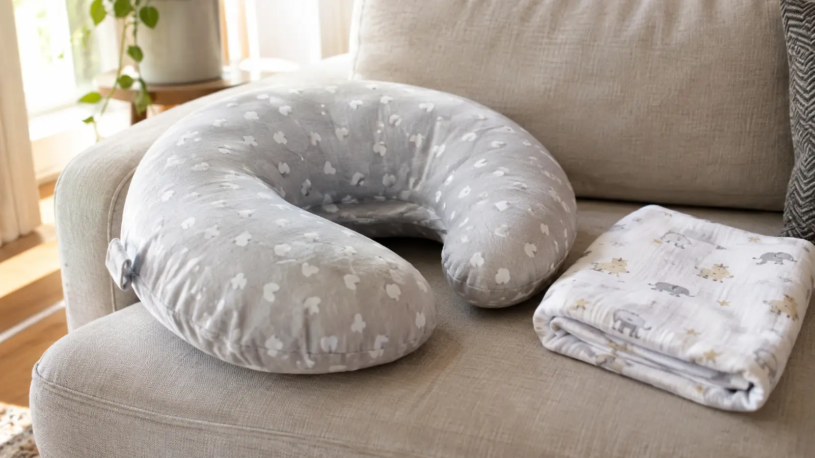A nursing pillow resting on a couch with a folded receiving blanket nearby